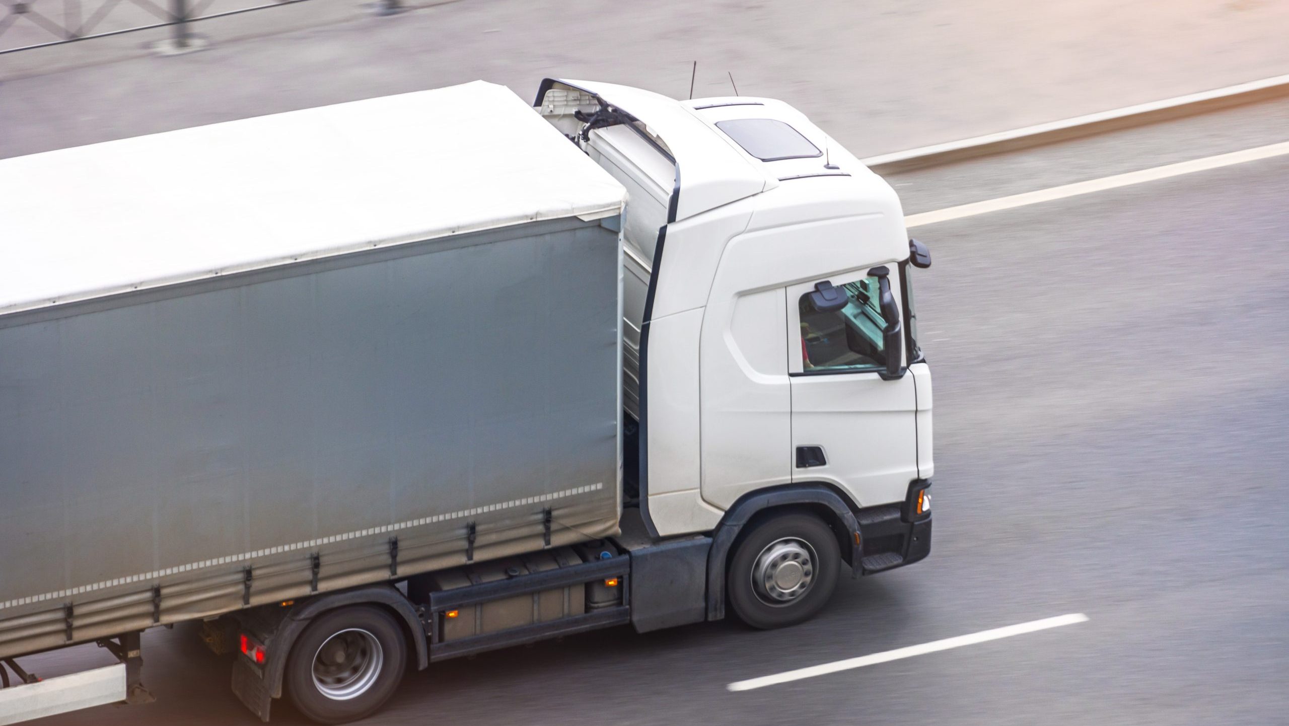 White truck with gray awning trailer rides on a city highway, side aerial view. DOGUTRUCK D6710 - Image 1